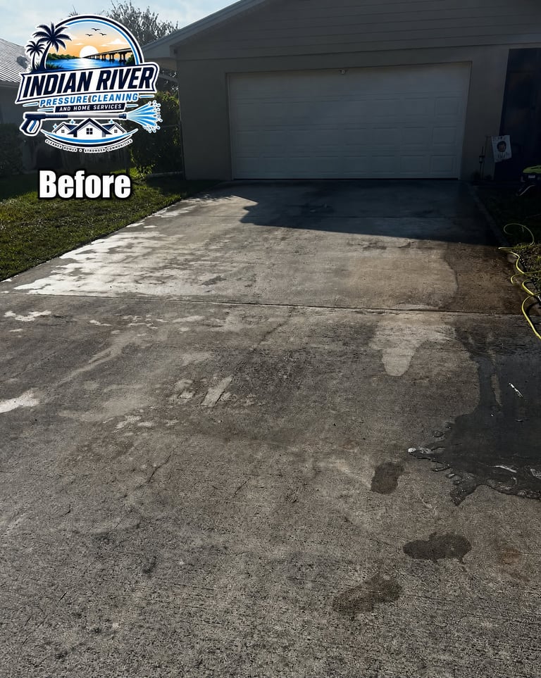 Before photo of dirty, stained concrete driveway with garage by Indian River pressure cleaning service