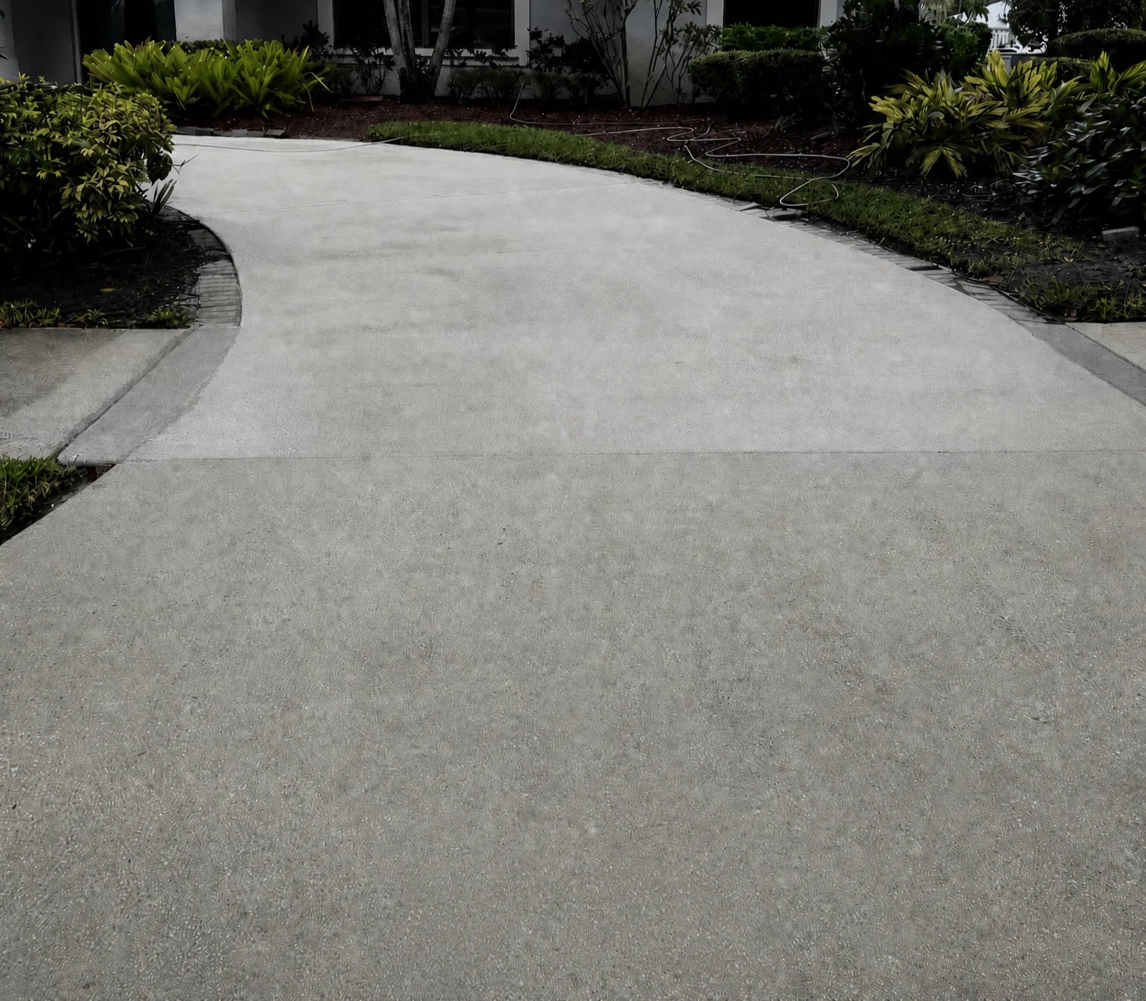 Curved concrete driveway lined with green landscaping and shrubs on both sides