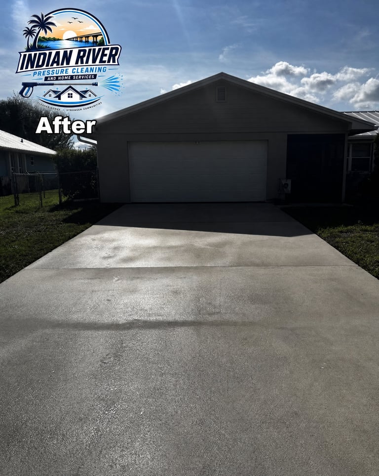 Clean concrete driveway in front of black garage with Indian River Pressure Cleaning logo overlay, showing after pressure washing results